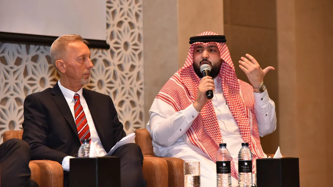 Two speakers in conversation on a panel stage, one answering into a microphone